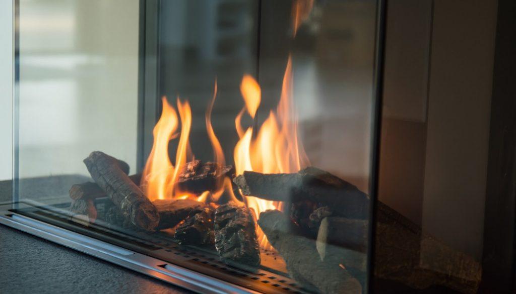 a fire burns in a glass fireplace, radiates heat